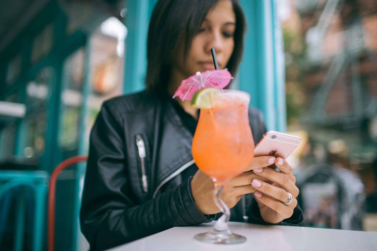 女人拿着鸡尾酒杯子在桌子上拿着手机