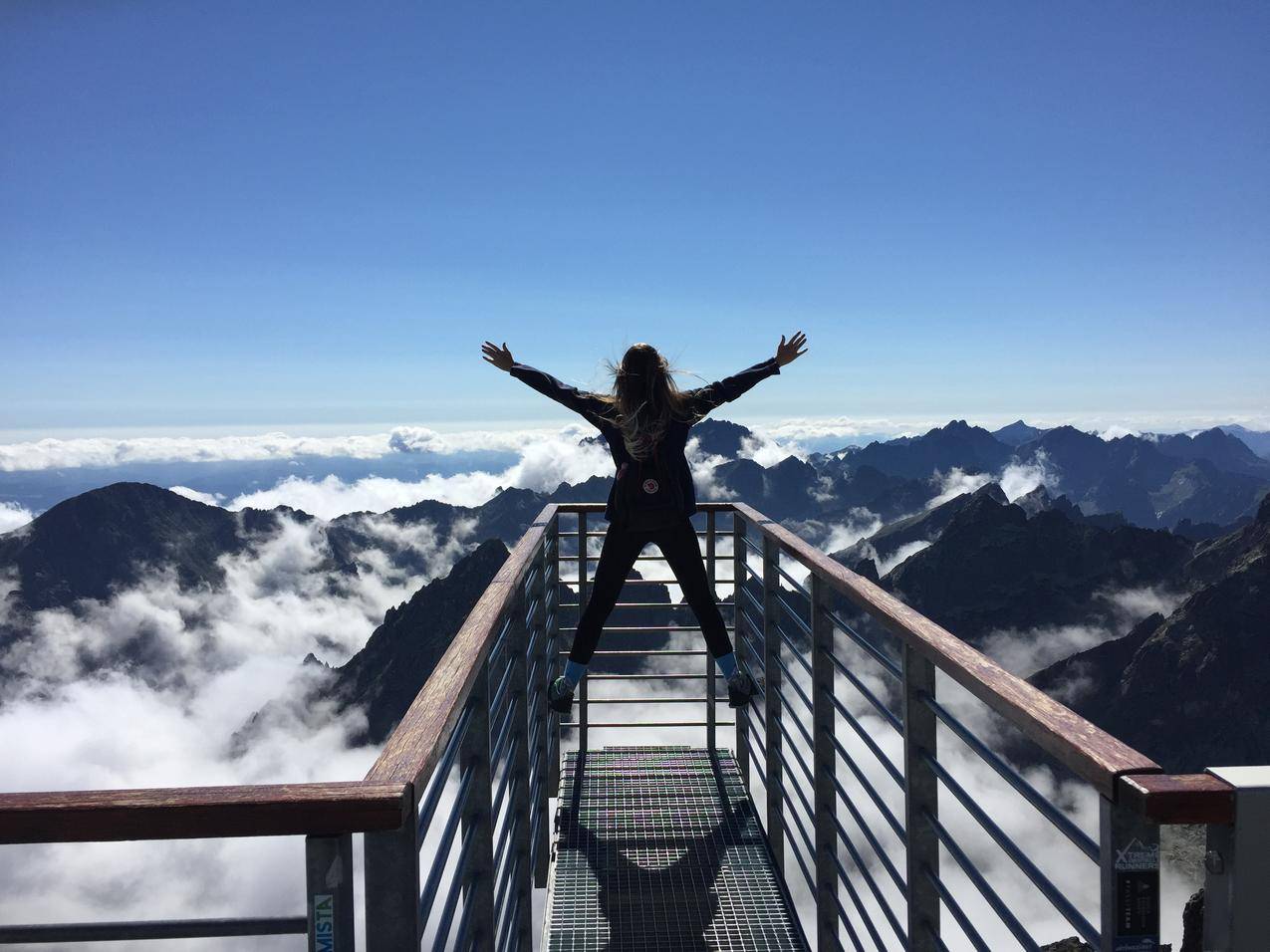 站在扶手上的人,张开双臂面对山峦和云层