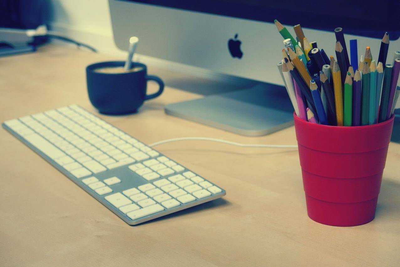 蓝绿色和黑色铅笔在红色塑料杯旁边的银IMAC