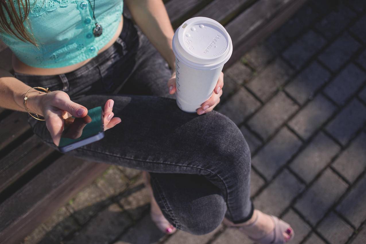 女士手持白色一次性杯子和智能手机