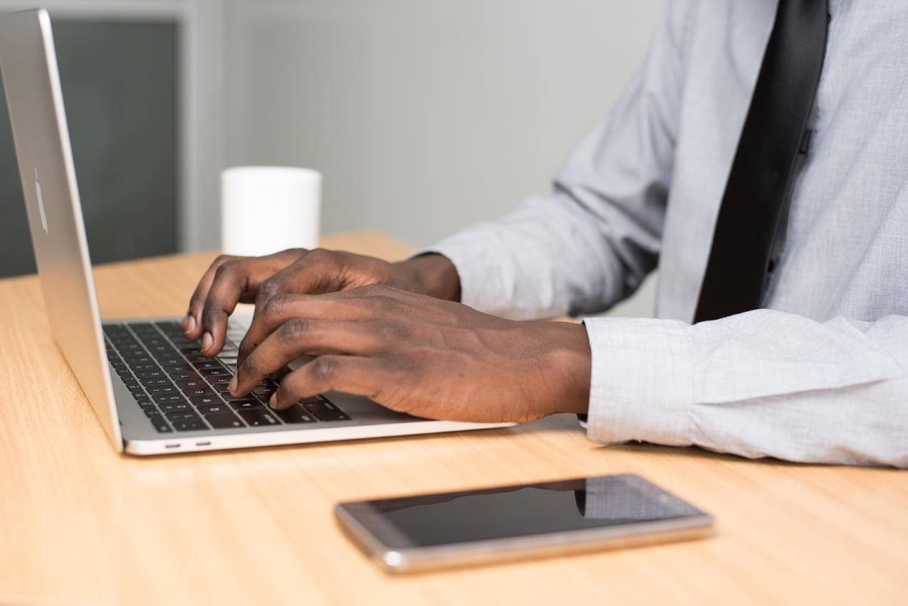 人Wearing,White穿着衬衫和黑色领带使用MacBook,Air在米色木桌上