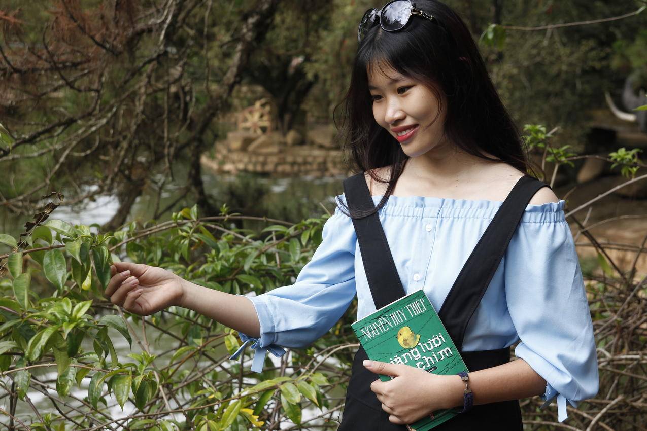 穿着蓝肩女衫的女人在绿叶植物旁边夹着书